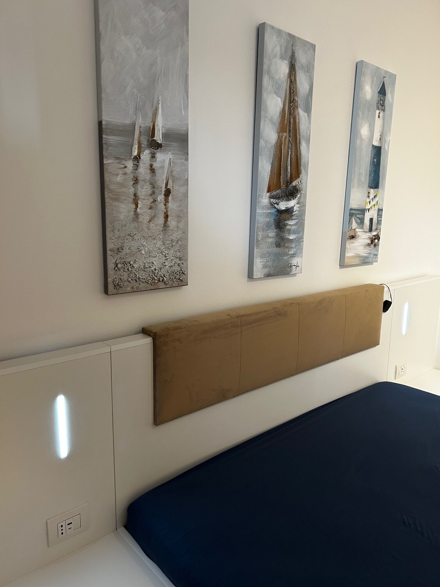 Quarto com uma cama, cabeceira de madeira e três quadros na parede.