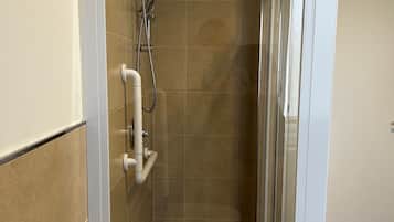 Un área de ducha pequeña y cerrada con puerta de vidrio, un cabezal de ducha y un rociador de mano.