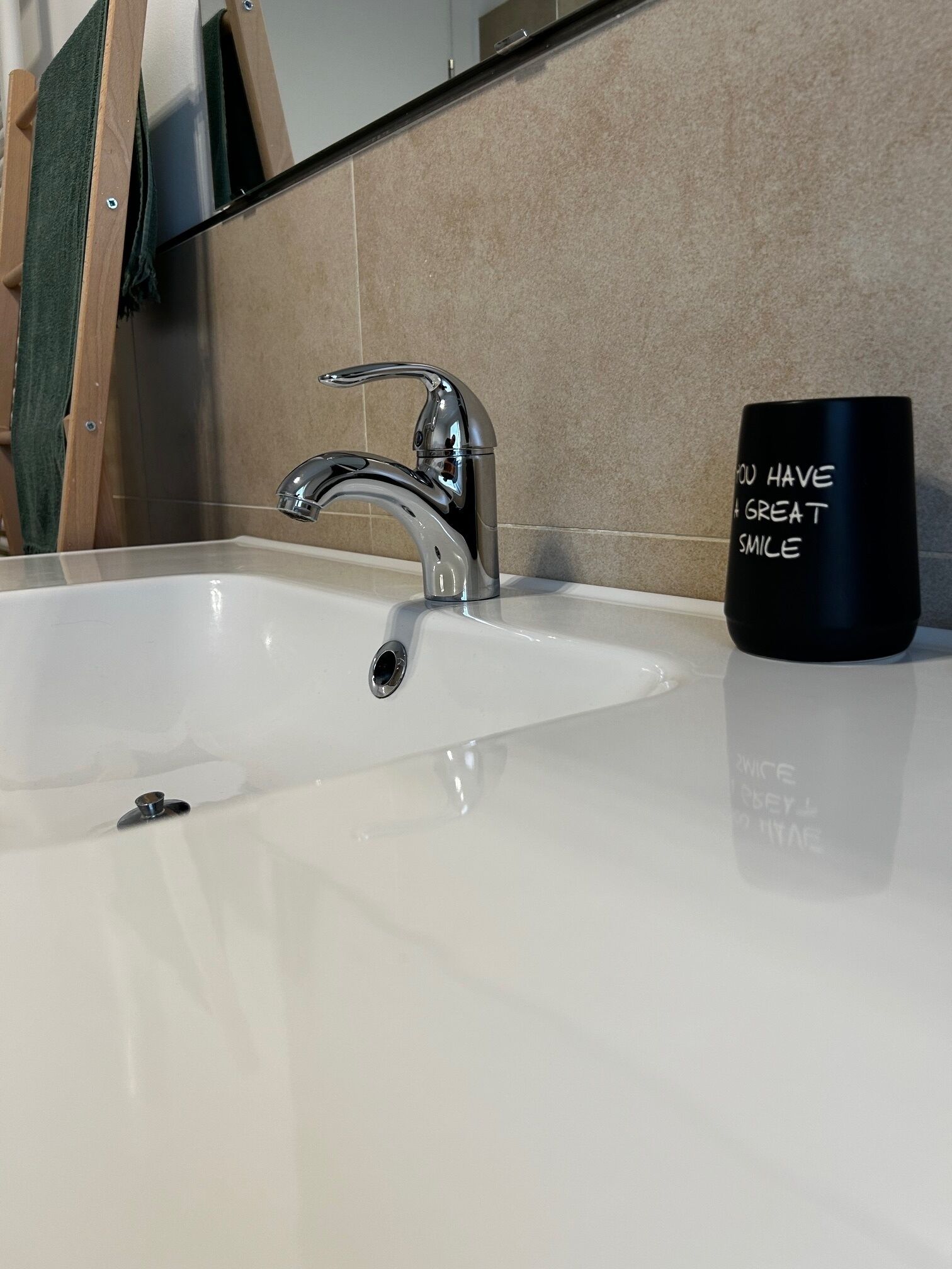 A bathroom sink with a modern faucet and a black mug with text.
