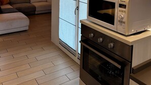 A compact kitchen with a microwave and oven, a sliding glass door, a framed picture on the wall, and a sofa in the adjacent living area. - A cozy and serene place for those seeking tranquility and comfort (Porpetto)