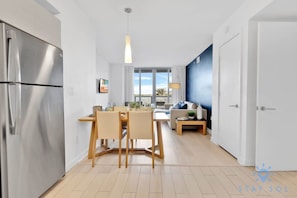 A modern kitchen with a stainless steel refrigerator, wooden dining table, and chairs.