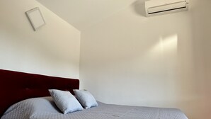 Un dormitorio con cama, almohadas, cabecera y un equipo de aire acondicionado en la pared.