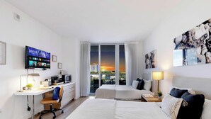 A hotel room with a bed, desk, TV, and a view of the sunset. - Studio - Resort & Pool - Gym (Hallandale Beach)