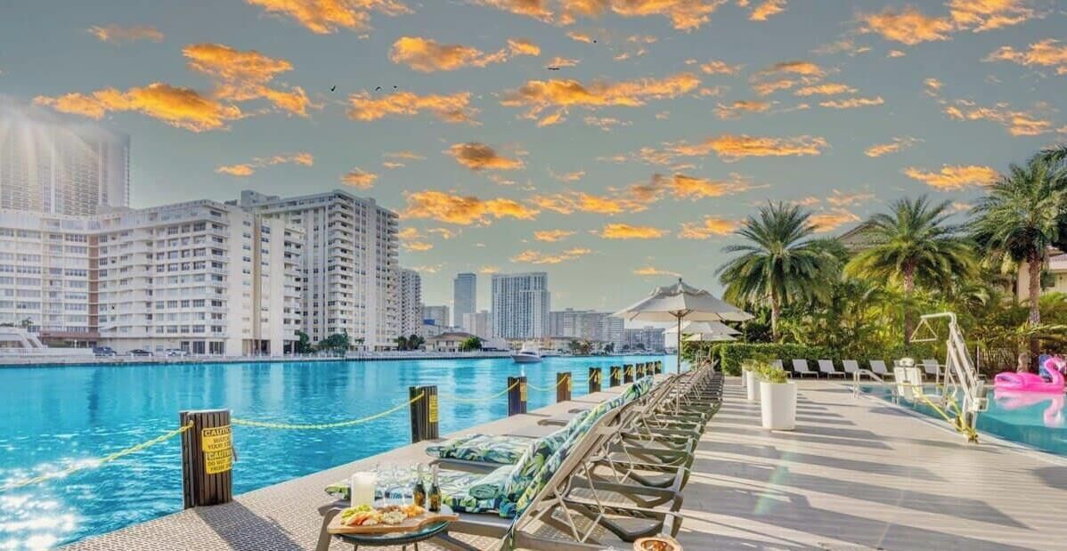 A poolside area with lounge chairs, a pool, and a city skyline in the background.