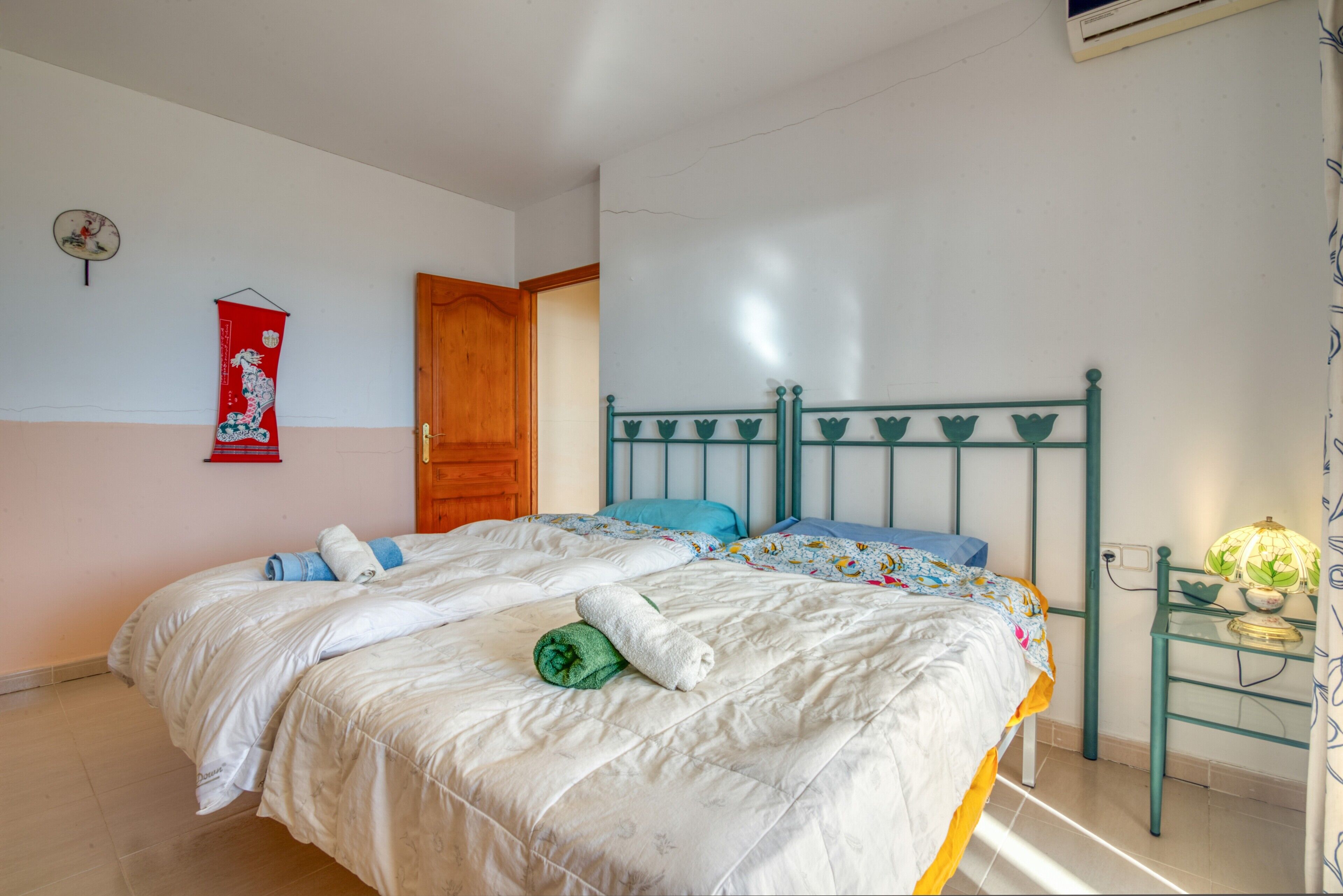 Un dormitorio con una cama, una puerta de madera, un reloj de pared y una pequeña mesa con lámpara.