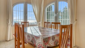 A dining area with a table and chairs, large windows, and curtains. - Villa 'Gaga Moraira' with Sea Views, Wi-Fi, and Air Conditioning (Teulada)