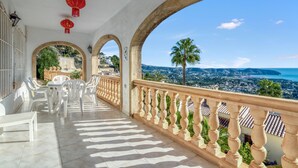 A balcony with white chairs and tables, a railing, and a view of a coastal city. - Villa 'Gaga Moraira' with Sea Views, Wi-Fi, and Air Conditioning (Teulada)