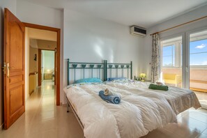 A bedroom with a bed, a wooden door, a hallway, and a balcony.