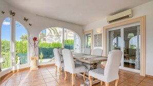 A dining area with a large table, chairs, and a view of greenery outside. - Villa 'Pinosol Con Vista Al Mar' with Sea View, Wi-Fi and Air Conditioning (Jávea)