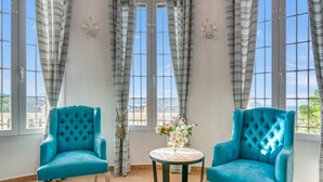 A room with two blue armchairs, a small round table with a vase of flowers, and large windows with curtains. - Villa 'Pinosol Con Vista Al Mar' with Sea View, Wi-Fi and Air Conditioning (Jávea)