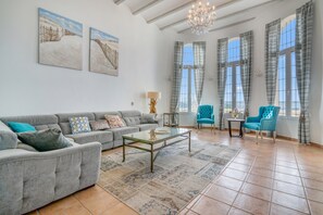 Een ruime woonkamer met een grijze bank, een glazen salontafel en twee blauwe fauteuils.