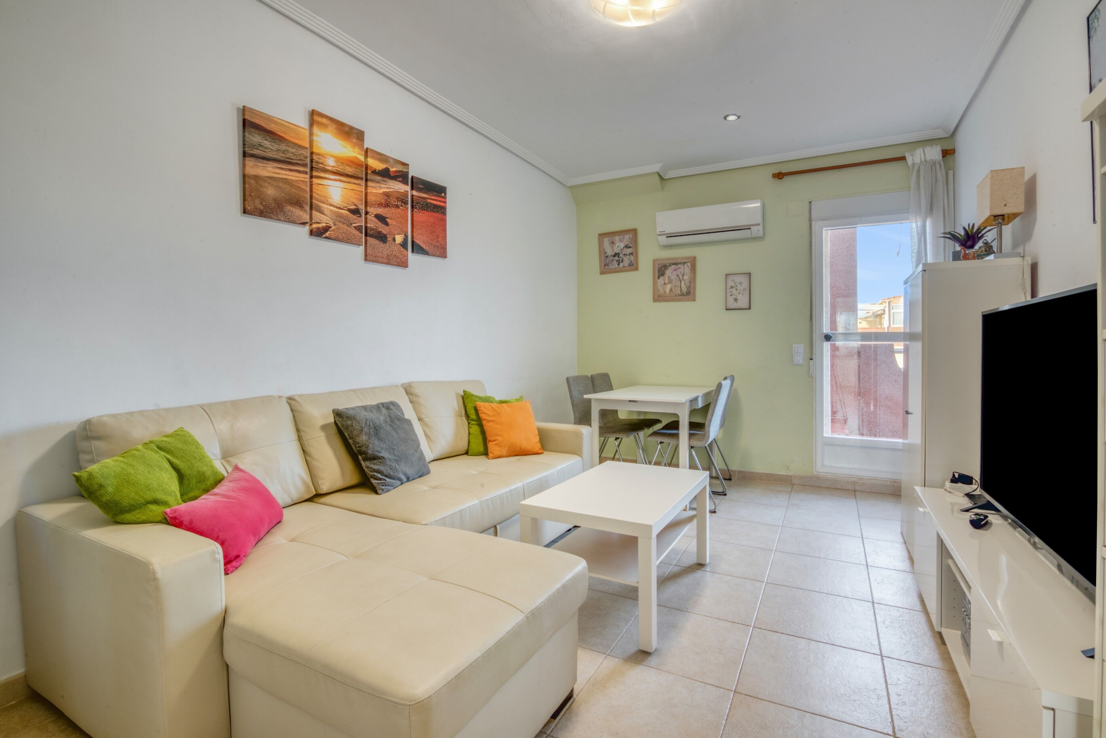 A living room with a sofa, a coffee table, a TV, and a dining area with chairs.