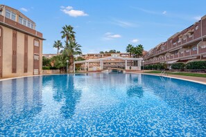 Une piscine dotée d’une terrasse carrelée, entourée d’immeubles avec balcons et de palmiers.