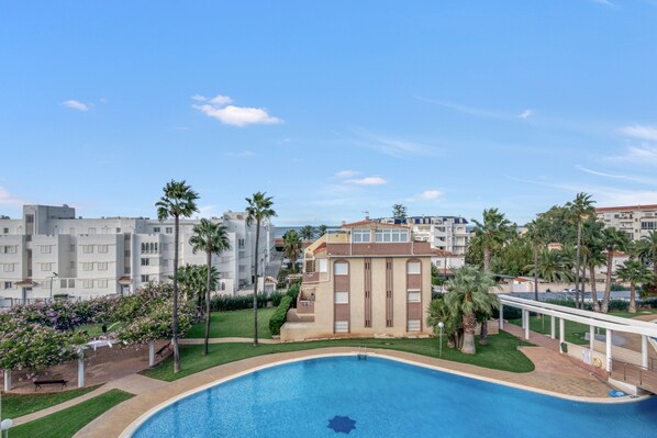 Une piscine entourée de palmiers et un bâtiment à la façade beige.