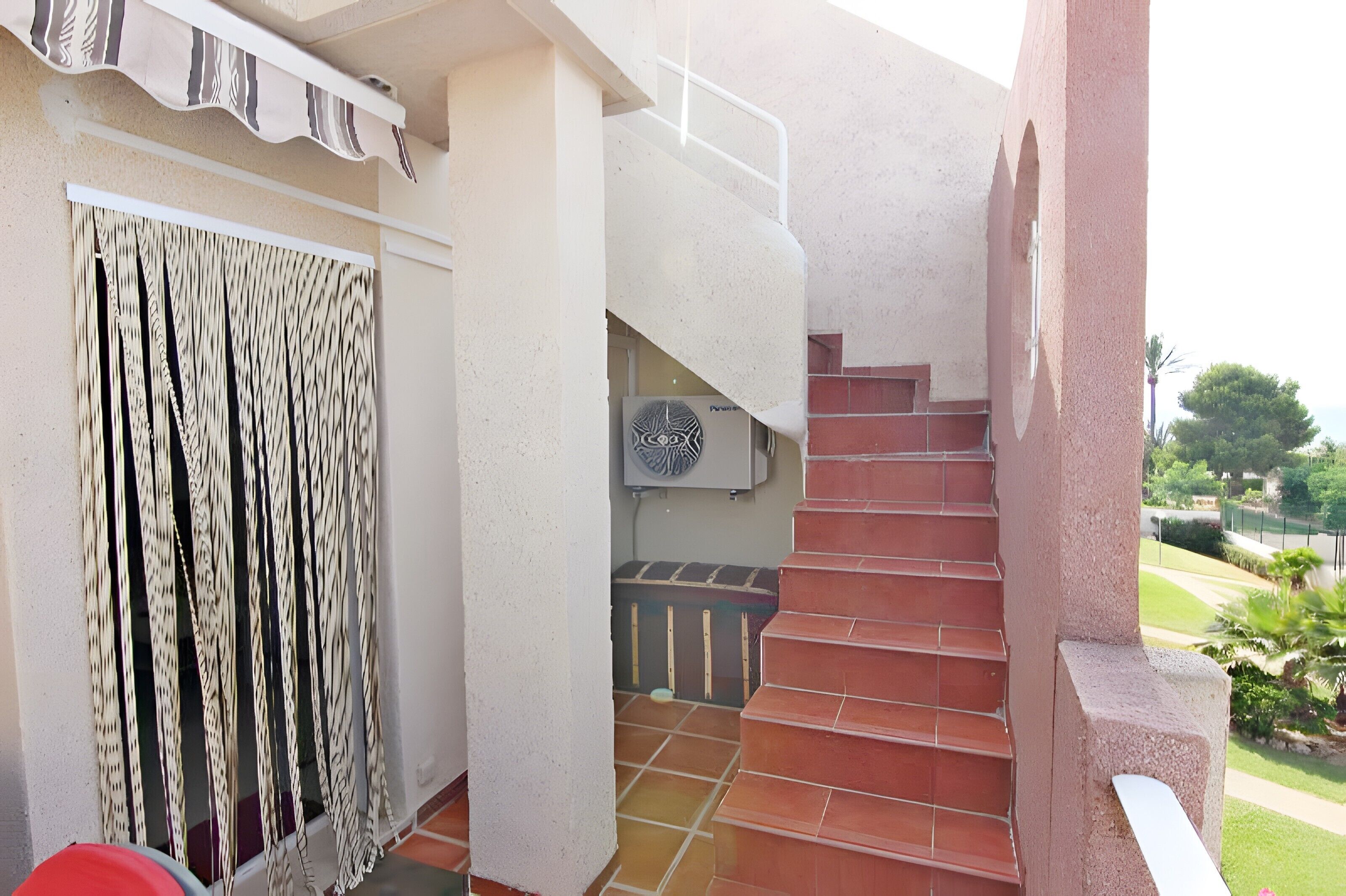 A staircase leading to a second floor, a window with patterned curtains, and an air conditioning unit.