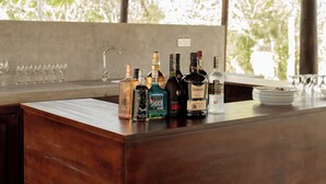 A bar area with various liquor bottles and glasses on a wooden counter. - Wilds Wilpattu (Pahala Maragahawewa)