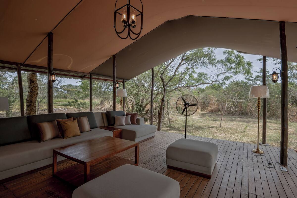 Un espacio al aire libre con mesa de madera, sofá con cojines y un ventilador.