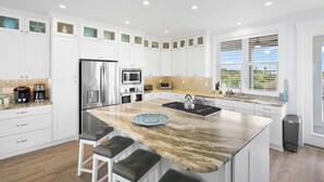 A modern kitchen with white cabinetry, a central island, stainless steel appliances, and a view of the outdoors. - Steps to Beach, Heated Pool, Elevator, Game Room (St. Augustine Beach)