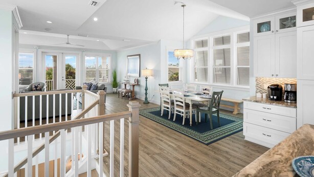 A spacious living area with a dining table, a kitchen with white cabinets, and a view of the outdoors. - Steps to Beach, Heated Pool, Elevator, Game Room (St. Augustine Beach)