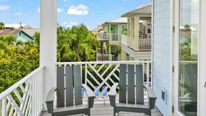 A covered porch with two Adirondack chairs, a white railing, and a view of neighboring buildings and greenery. - Steps to Beach, Heated Pool, Elevator, Game Room (St. Augustine Beach)