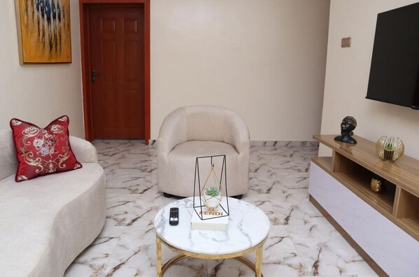 A living room with a sofa, armchair, coffee table, and a TV mounted on the wall. - Opal Selfie Apartment in Lagos (Lagos)