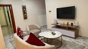 A living room with a sofa, a coffee table, a flat-screen TV, and a marble floor.