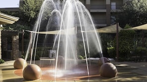 A water feature with multiple streams, surrounded by spherical bollards and a covered seating area.