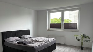 Een slaapkamer met een bed, een raam met zonwering, een radiator en een kamerplant.