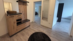 Een moderne woonkamer met een houten tv-meubel, een grote spiegel en een donker vloerkleed.
