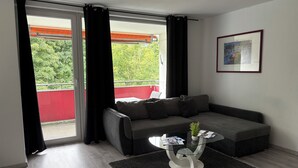 Een moderne woonkamer met een grijze bank, een glazen salontafel en een zwart vloerkleed.