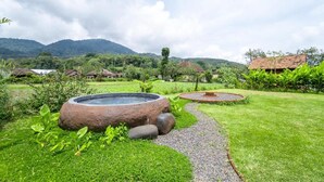 Un jardín con una fuente de piedra circular, un sendero de grava y vistas a casas al fondo.