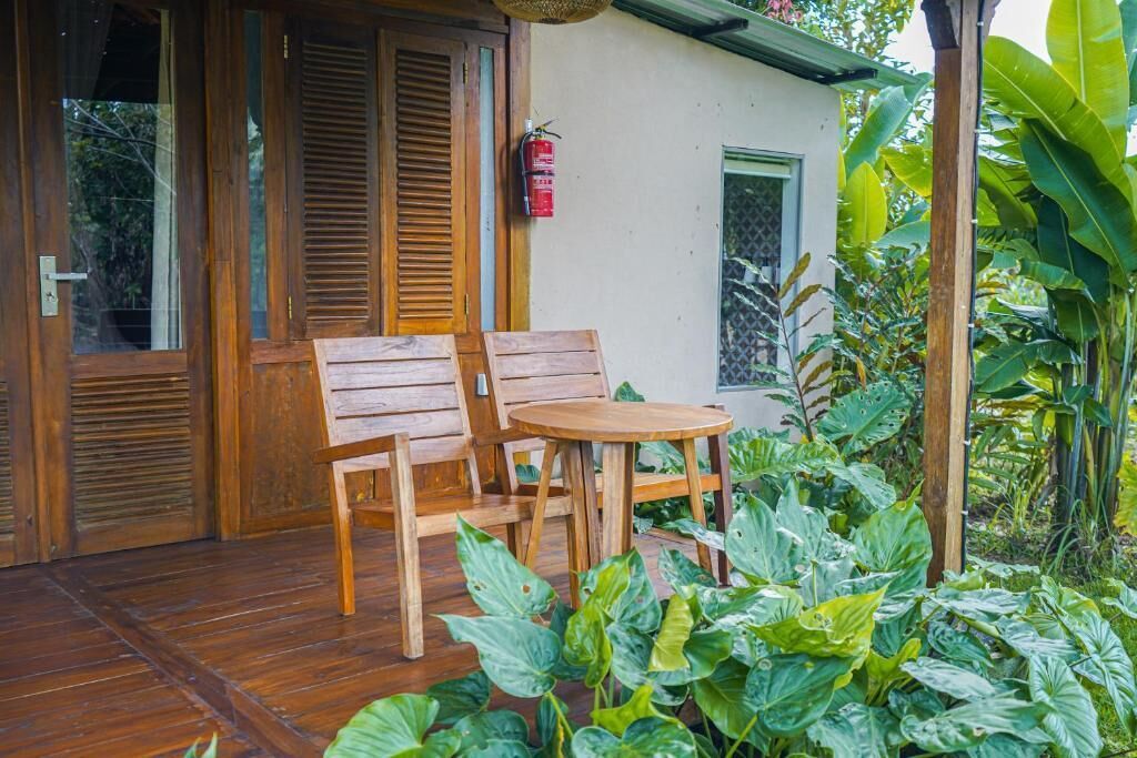 A wooden porch with a table and chairs, surrounded by lush green plants.