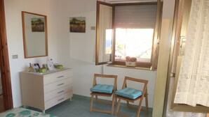 A bedroom with a bed, a dresser, two chairs, a window with a view, and a door.