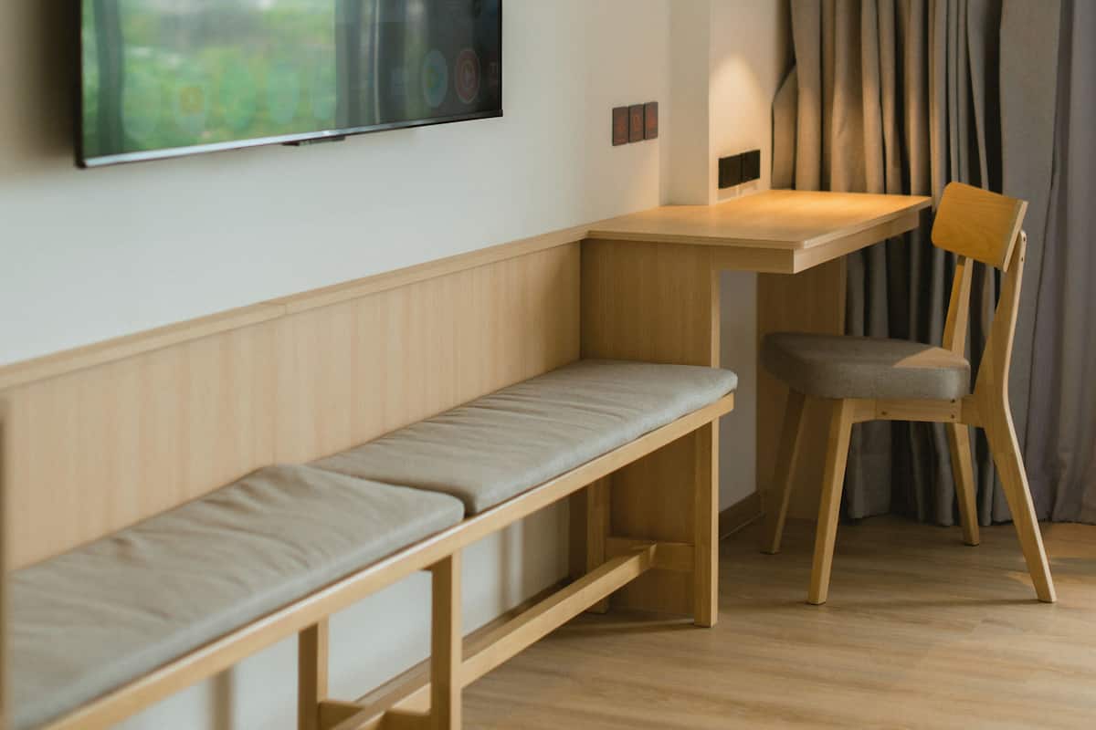 A modern room with a wooden desk, a bench, and a large flat-screen TV mounted on the wall.