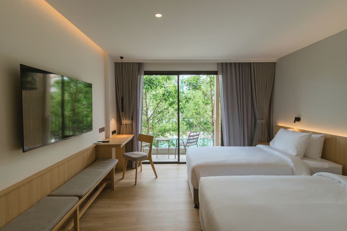 A hotel room with a large bed, a desk with a chair, a bench, and a TV on the wall.