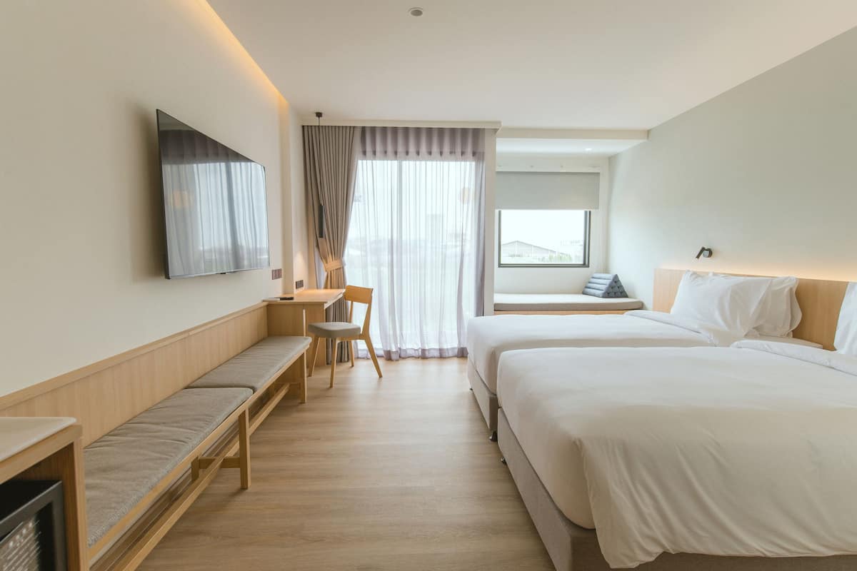 A hotel room with two beds, a desk, a chair, a TV, and a window with curtains.