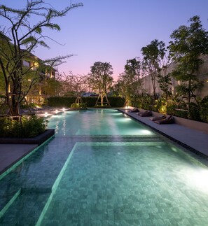 A swimming pool with clear water, surrounded by trees and buildings. - PAAK Hotel Suvarnabhumi (Bangkok)