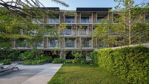 Un immeuble moderne à plusieurs étages, doté de balcons, entouré d’une végétation luxuriante et d’une pelouse bien entretenue.