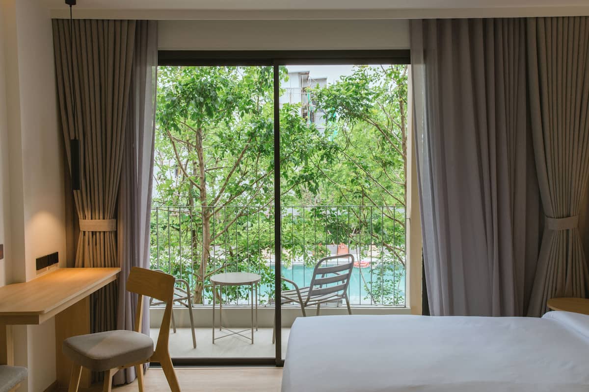 A hotel room with a bed, a desk, and a chair. There is a view of a pool and trees outside the window.