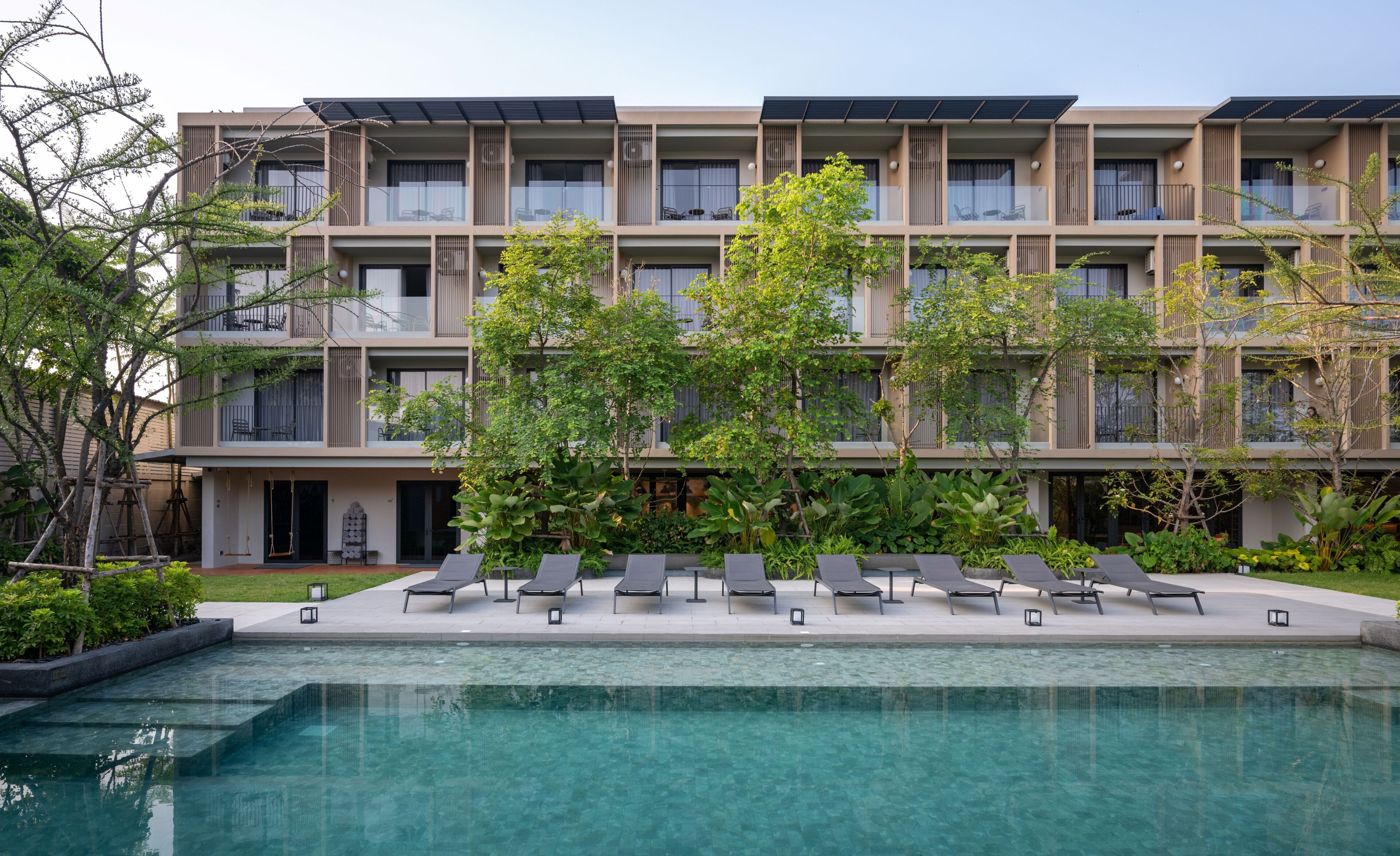 A modern hotel with a pool, lounge chairs, and a garden area.
