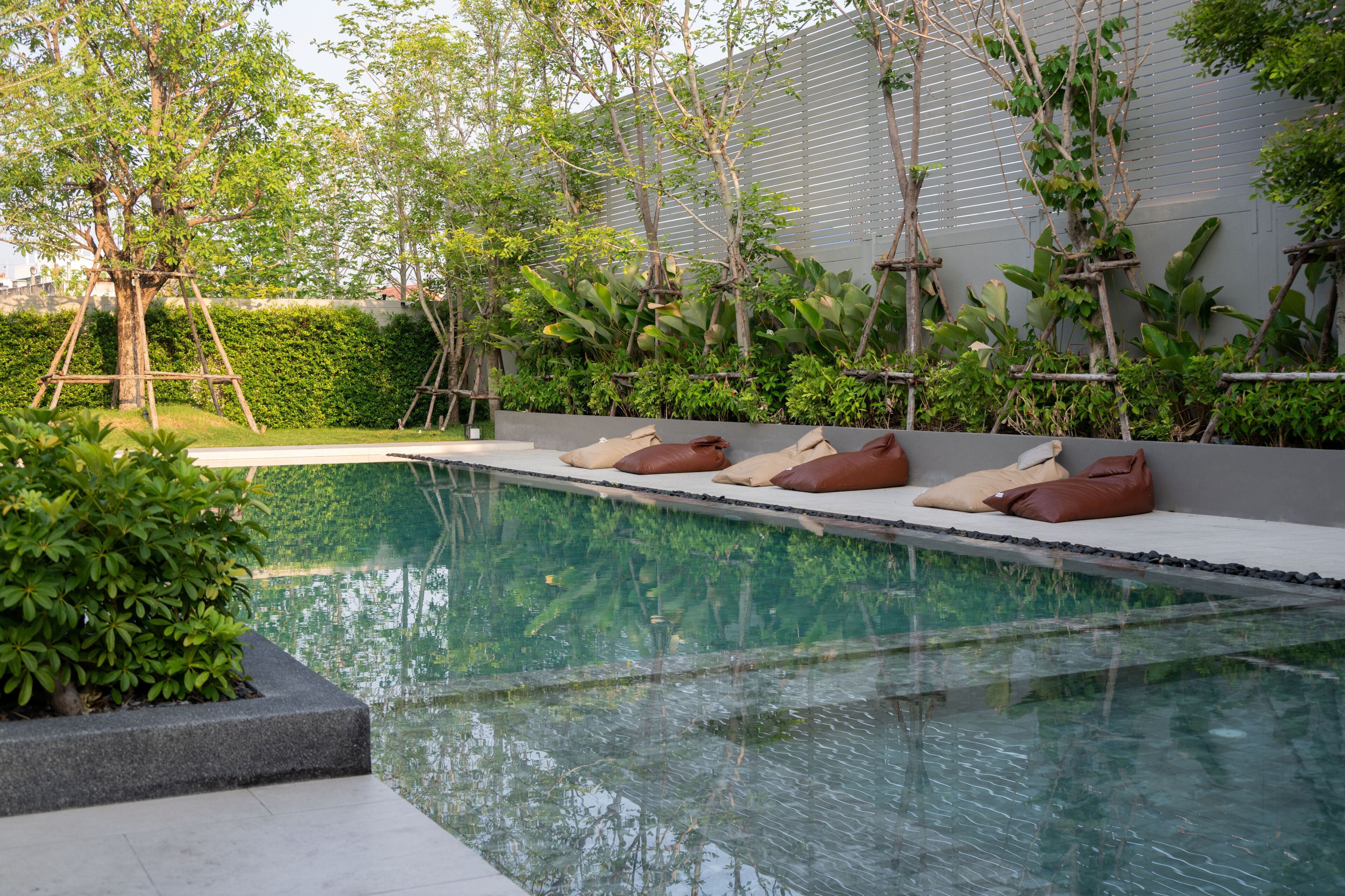 A swimming pool with a seating area, surrounded by greenery and a hedge.