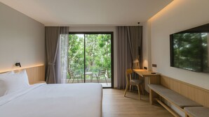 Une chambre d’hôtel moderne, dotée d’un grand lit, d’un bureau, d’une banquette et offrant une vue sur la verdure par la fenêtre.