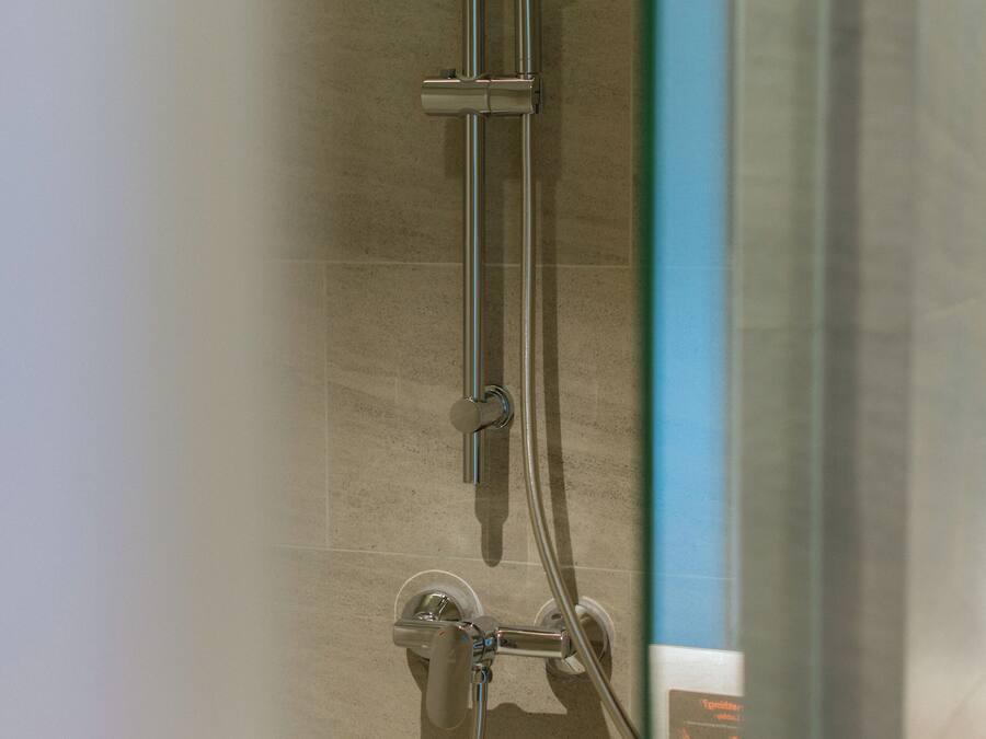 A shower with a handheld showerhead and a wall-mounted control panel.