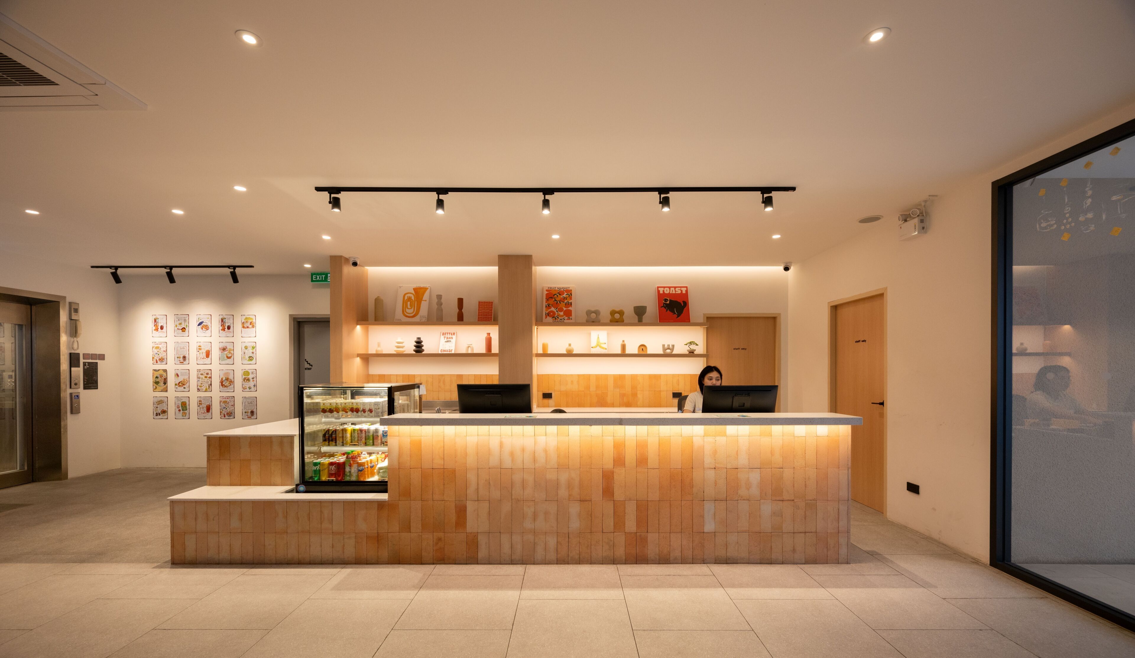 A reception area with a counter, a refrigerator with beverages, and a wall with various items.