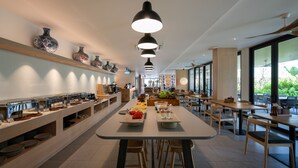 Un espace repas moderne avec plusieurs tables et chaises, un buffet proposant divers plats et des vases décoratifs accrochés au mur.