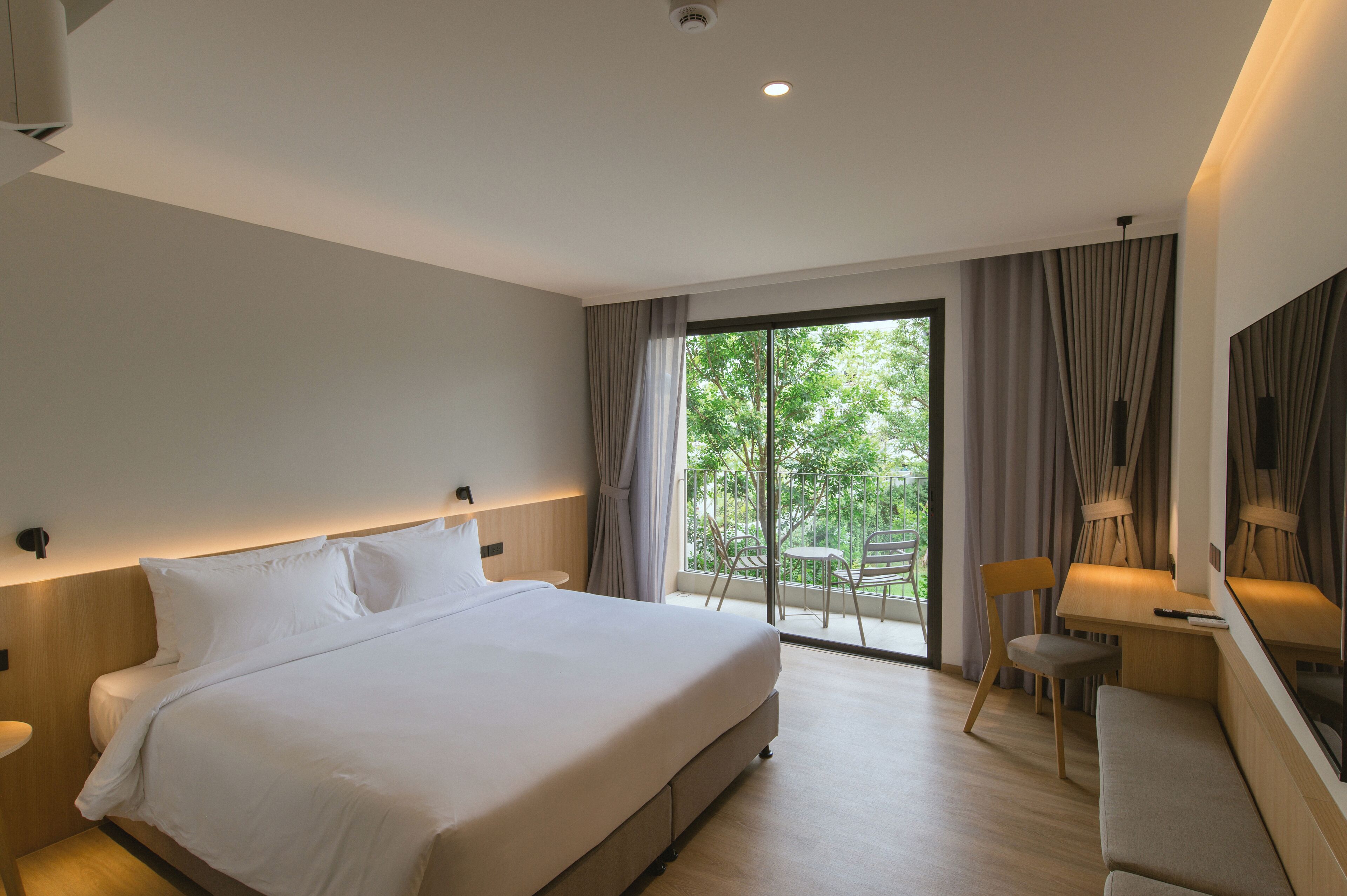 Una habitación de hotel moderna con una cama grande, un escritorio y un balcón con sillas.