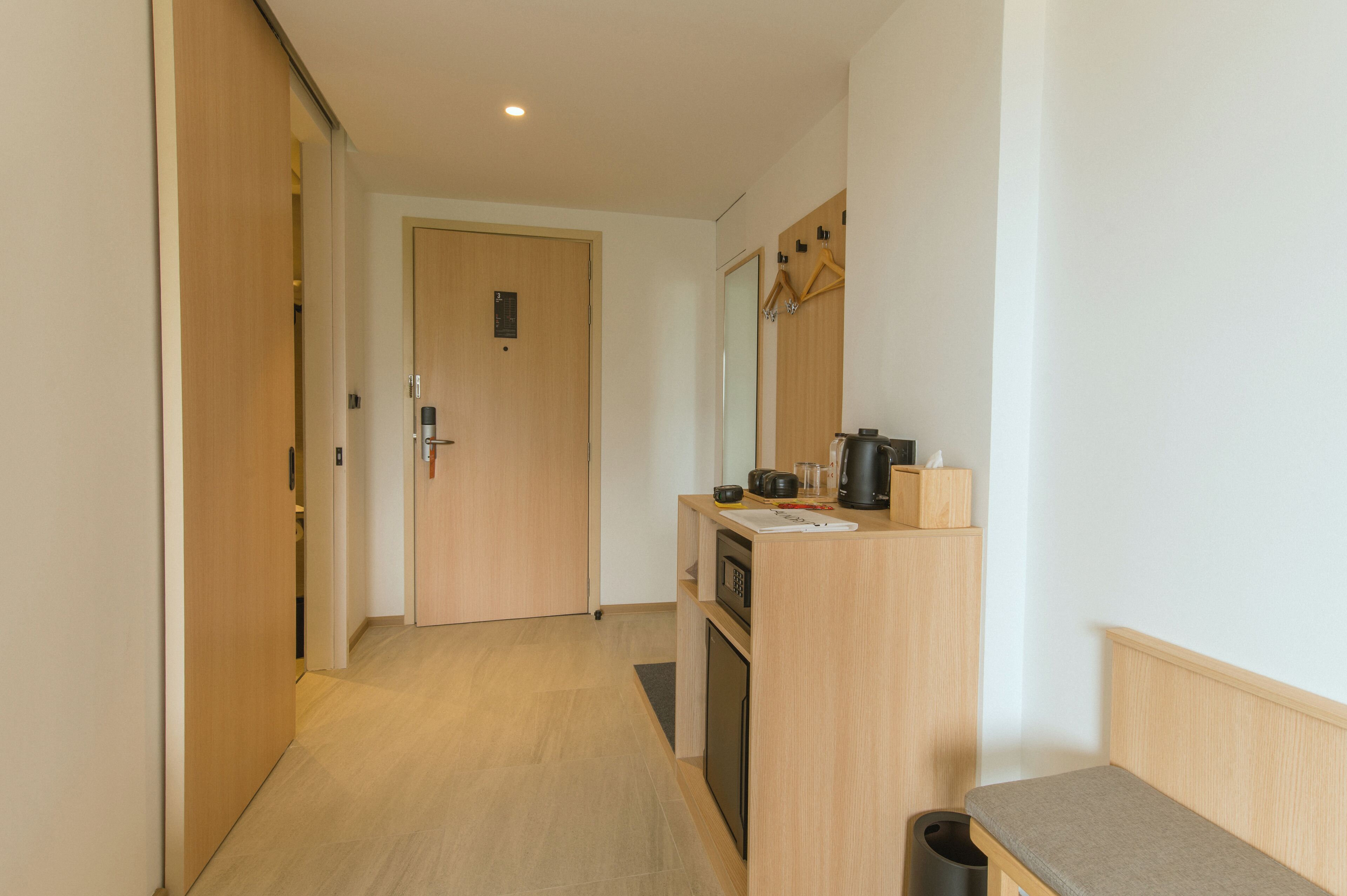 Un pasillo con una puerta de madera, una kitchenette con microondas, cafetera y un pequeño bote de basura.