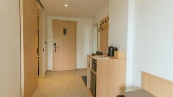 Un pasillo con una puerta de madera, una kitchenette con microondas, cafetera y un pequeño bote de basura.