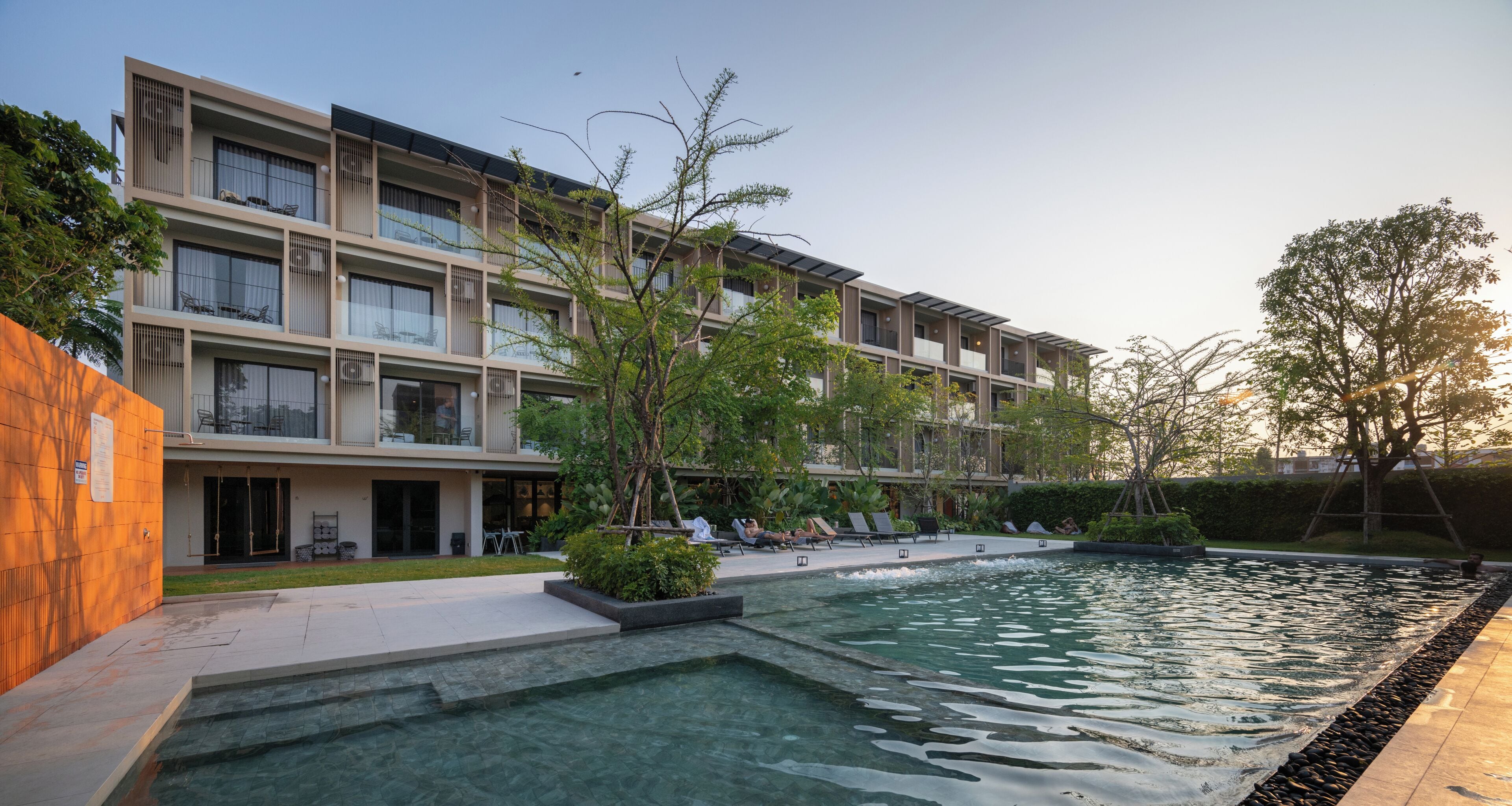 A modern building with multiple balconies, a swimming pool, and outdoor seating areas.