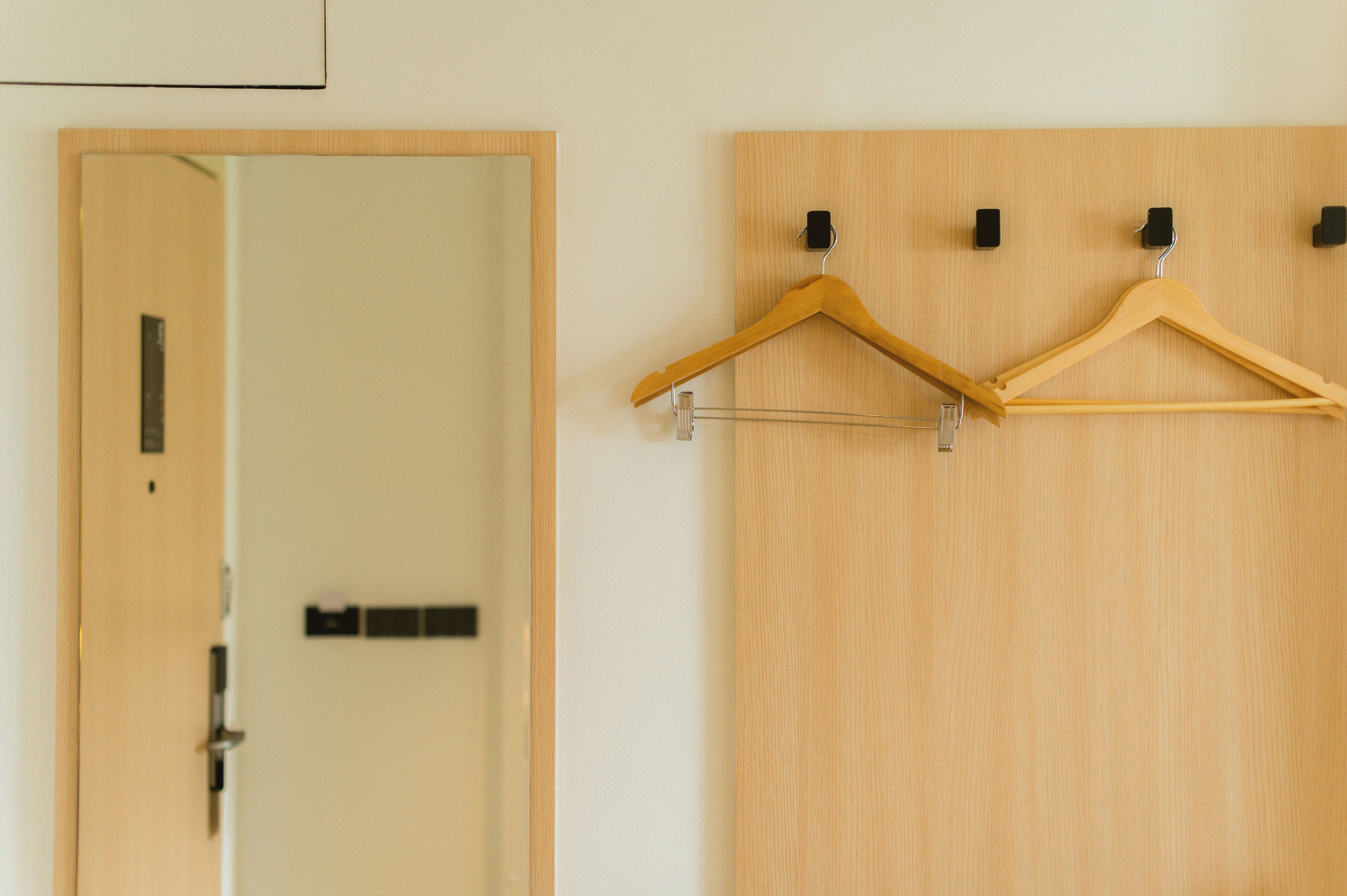 Une porte en bois avec un miroir et deux cintres en bois dotés de pinces noires.